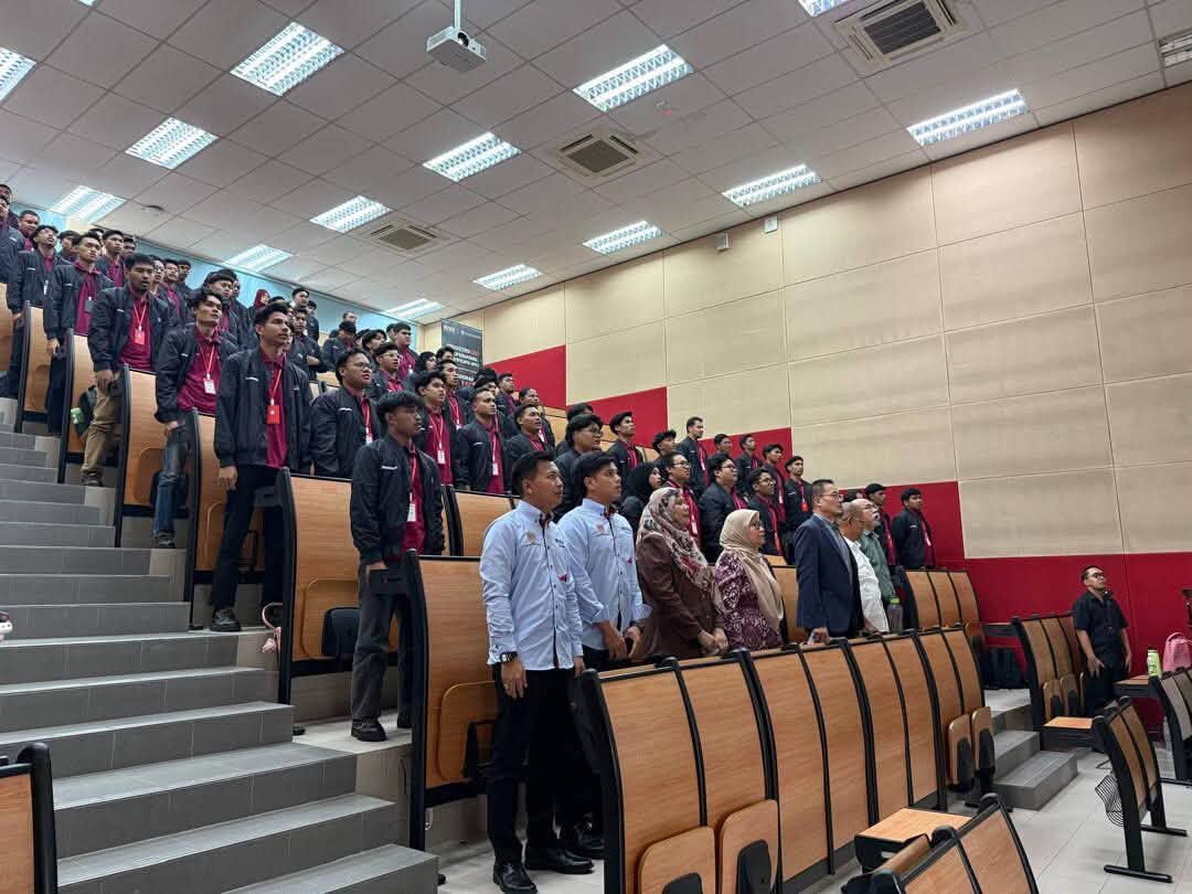 Peserta Batch 1 & 2 berjaket seragam di tingkat dewan kuliah, dengan tetamu berdiri di hadapan